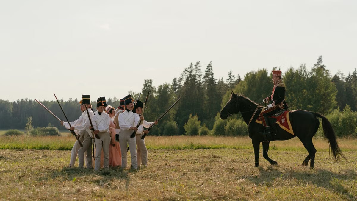 Men in historical uniforms and soldier on horseback reenact a battle scene outdoors.